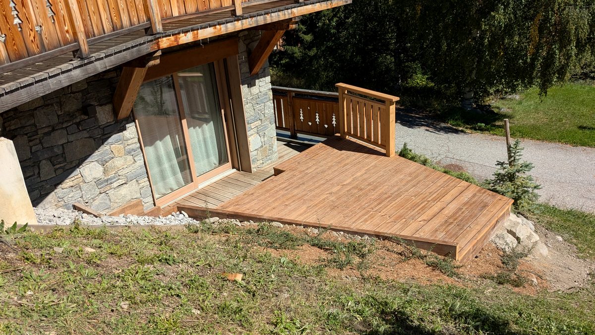 La terrasse en bois finie, posée sur la pente devant la baie du chalet